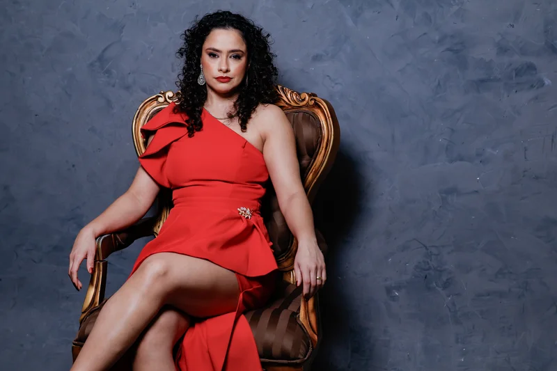 Retrato de uma mulher com vestido vermelho sentada em uma cadeira de madeira.