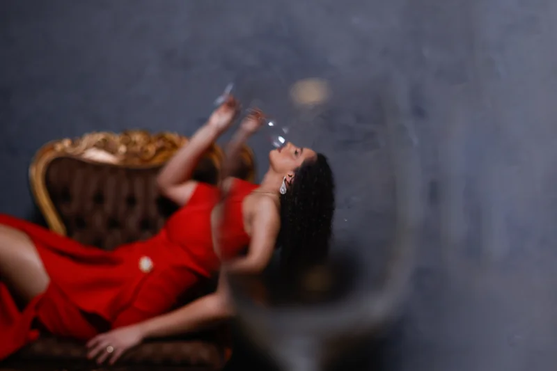 Retrato de uma mulher com vestido vermelho deitada nos braços de uma cadeira através de uma taça.