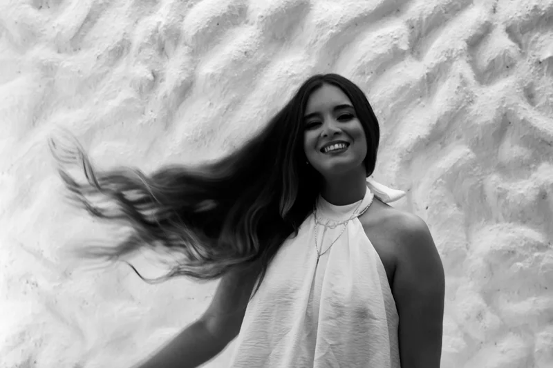Retrato monocromático de uma mulher com vestido branco jogando os cabelos de lado.